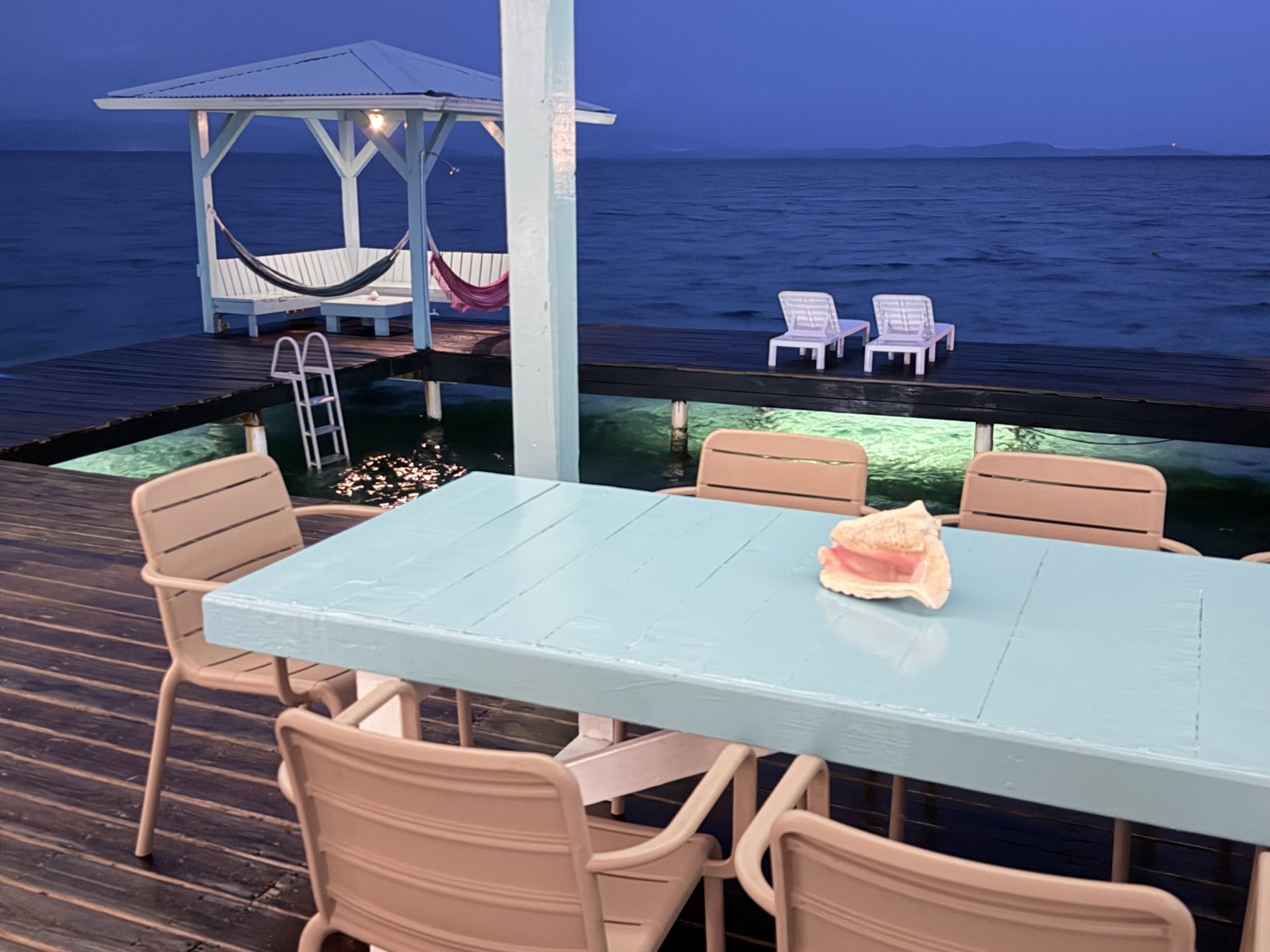 Dining table on the deck at dusk, with the gazebo, hammocks and lit water beyond